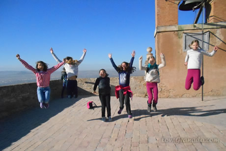 a group of children jumping next to bell tower in the alhambra